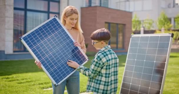 妈妈拿着太阳能电池板和儿子说话母亲和儿子在太阳能电池板附近 小男孩仔细地看着太阳能电池板 把阳光转化为电 生态意识概念 — 图库视频影像