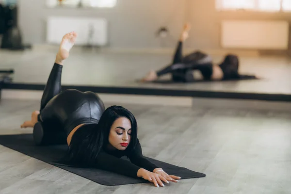 一名身穿黑色运动服的妇女躺在地板上 在家里练习阿萨纳舞 这有助于减轻腰痛 这是初学者的一种灵活的身体伸展 — 图库照片