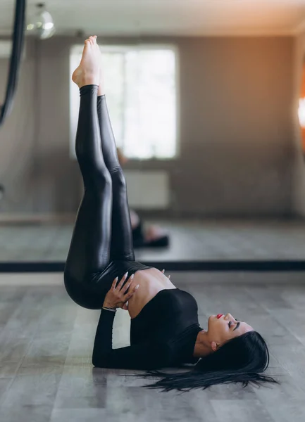 做运动的女人穿着深色运动服的黑发女子正在做瑜伽或健身锻炼 她仰卧在床上 双腿翘起 双手放在腰部 — 图库照片