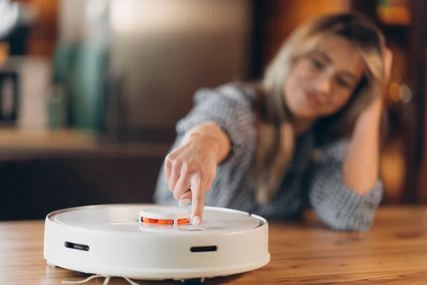 Robot vacuum cleaner with lidar sensor, woman turns it on. blurred background. place for inserting text. smart home concept.