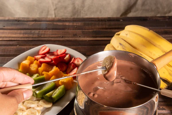 stock image chocolate fondue accompanied by tropical fruits on wooden table and dark background