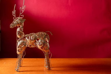 Geyik şekilli Noel süsü, gümüş parıltısıyla kaplanmış, kırmızı arka planda duruyor...