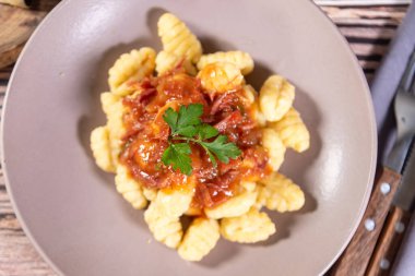 Yanında parmesan peynirli Gnocchi, ahşap bir masada domates sosu ve etrafında hazırlık bileşenleri var.
