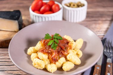 Yanında parmesan peynirli Gnocchi, ahşap bir masada domates sosu ve etrafında hazırlık bileşenleri var.