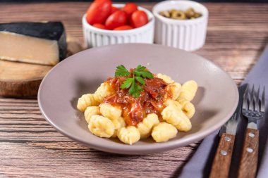 Yanında parmesan peynirli Gnocchi, ahşap bir masada domates sosu ve etrafında hazırlık bileşenleri var.