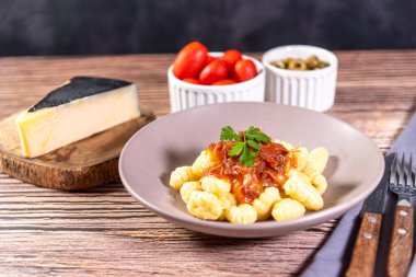 Yanında parmesan peynirli Gnocchi, ahşap bir masada domates sosu ve etrafında hazırlık bileşenleri var.