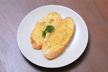 Beyaz tabakta çıtır sarımsaklı ekmek. Tereyağlı, sarımsaklı ve maydanozlu ekmek. 