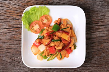 Stir-fried chicken with cashew nuts in white plate on old wooden board 