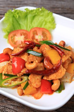 Stir-fried chicken with cashew nuts in white plate on old wooden board 