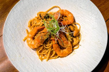 Lezzetli kaplan karidesleri ve dolgun midyeler mükemmel pişirilmiş bir spagetti yığınını güzelce süslüyor ve temiz beyaz bir tabakta sunuluyor. Yakın plan fotoğraf. Seçici odak.