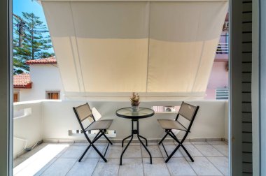 Dışarıdaki balkonda modern mobilya masası ve rahatlamak için iki sandalye, kahvaltı, öğle yemeği ve akşam yemeği var.. 