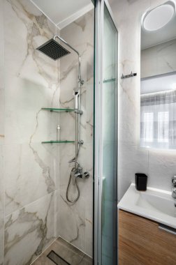 Beyaz ve gri renkli modern fayanslı banyo. Cam bölmeli duş kabini, yağmur duşu, beyaz lavabo için ahşap standı ve duvarında ayna var. Seçici odak