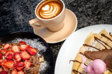 Yanında Waffle ve Pancake 'le birlikte Cappuccino' nun yakın çekimi. Kahvaltı, brunch ya da kahve dükkanı temalı projeler için idealdir. Bu yüksek çözünürlüklü resim davetkar detayları yakalar. .