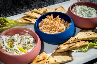 İçinde dilimlenmiş pita ekmeği, üç farklı soslu Yunan yoğurdu, tzatziki ve cezbedici üçüncü bir seçenek de bulunan soğuk atıştırmalıklarla dolu bir tabak. Aperatifler ve Akdeniz aşıkları için mükemmel..