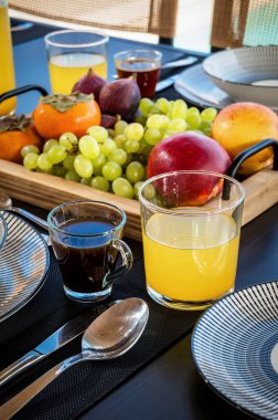 Davetli Kahvaltı Konsepti: Bir fincan dumanı tüten kahve, ferahlatıcı bir bardak meyve suyu ve çeşitli meyvelerle dolu bir sepet içeren güzel bir set masası. 