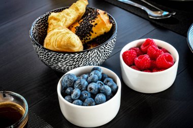 Lezzetli Üçlü: Taze pişmiş çörekler, yabanmersinleri ve ahududularla dolup taşan Beyaz Kâselerin Yakın Çekimi. Mutfak, yemek ya da yaşam tarzı temalı projeler için ideal seçim.