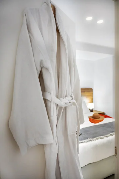 White Bathrobe Hanging in Bedroom Background: Relaxing and Cozy Atmosphere. Perfect for use in home decor publications, hospitality promotions, and lifestyle concepts. A touch of comfort and luxury.