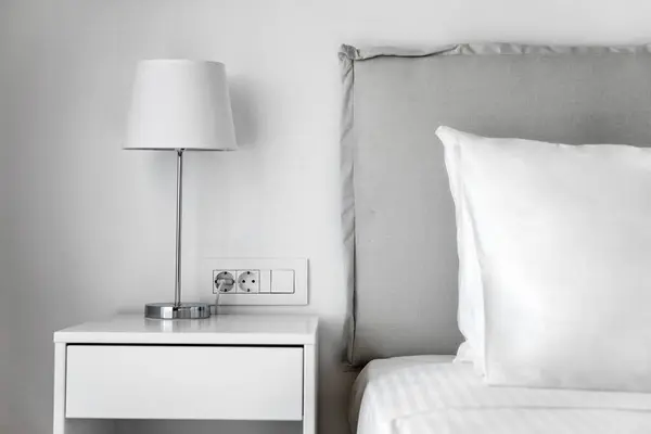 Minimalist Bedroom Concept: White Bedding, Pillow, and Bedside Table with Lamp.  Perfect for use in home decor publications, interior design concepts, and lifestyle promotions.