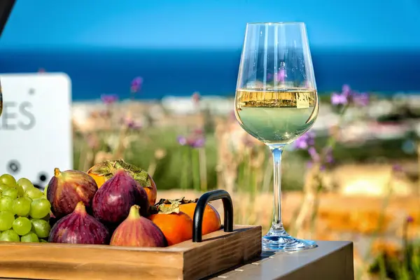 Summer Delight: Close-Up of White Wine Glass and Fresh Fruits on Tray with Idyllic Seaside blurred Background. ideal choice for conveying the refreshing and luxurious ambiance of a summer retreat