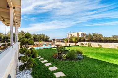 Özel bir villanın ya da evin bahçe planında dairesel şekillerde şekillendirilmiş ağaçlarla süslenmiş yeşil bir çimen sergileniyor..