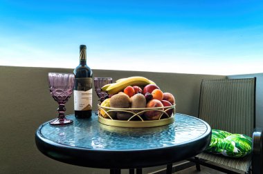 Girit, Yunanistan-6.7.2024: kayısı, şeftali, kivi ve muzla dolu vazonun yakın çekimi. Arka plandaki bulanık şarap ve bardaklar çekici bir atmosfer olduğunu gösteriyor.