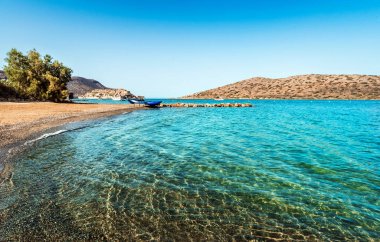 Şeffaf mavi sularla açık deniz hattının yer aldığı canlı bir yaz sahnesi, çakıl taşlı tabanı gözler önüne seriyor. Parlak güneş ışığı suyun doğal güzelliğini arttırır, ferahlatıcı ve davetkar bir atmosfer yaratır.