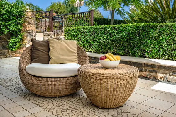 Stock image Cozy backyard featuring elegant rattan furniture, including armchair and table, served with fruits. Outside interior design combining comfort and style in serene environment, perfect for relaxation.