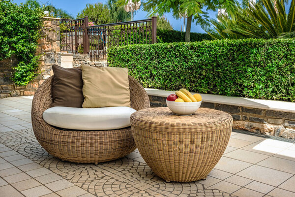 Cozy backyard featuring elegant rattan furniture, including armchair and table, served with fruits. Outside interior design combining comfort and style in serene environment, perfect for relaxation.