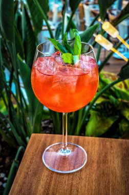 İçi Aperol Spritz dolu cam yakın plan. Canlı turuncu-kırmızı renkli, içinde görünür kabarcıklar ve turuncu dilimler var. Bardak buzla dolu, serin ve ferahlatıcı bir görünüm yaratıyor.