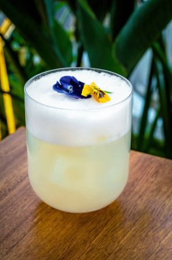 Lowball bardağı açık sarı bir kokteyl ile dolduruldu, üzeri yumurta beyazı köpükle kaplandı ve narin çiçeklerle süslendi. Zarif ve görsel olarak çekici. 