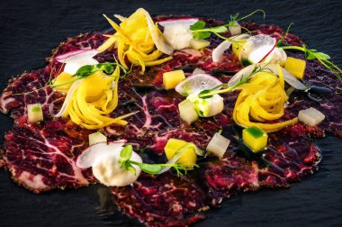 Zarif ve şık bir restoran yemeği, el değmemiş tabakta güzel bir şekilde sunulur. Tabak ince, büyük bir dilim taze siyah Angus tartar içeriyor, ustalıkla hazırlanmış, üzerinde canlı sebze süslemeleri var.