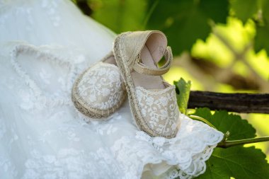 Close-up of girls' shoes in beige tones on white dress meant for baptizing. Shoes feature simple, elegant design matching the purity of baptismal clothing. Soft lighting highlights textures  clipart