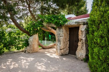 Taş girişi, yemyeşil, küçük ve büyüleyici bir kiliseye açılıyor. Manzara aydınlık ve huzurlu, güneş ışığı kiliseyi aydınlatıyor ve etraf canlı yapraklarla dolu, dingin ve davetkar.