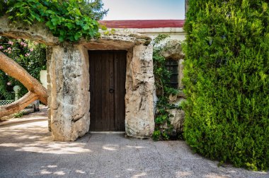 Taş girişi, yemyeşil, küçük ve büyüleyici bir kiliseye açılıyor. Manzara aydınlık ve huzurlu, güneş ışığı kiliseyi aydınlatıyor ve etraf canlı yapraklarla dolu, dingin ve davetkar.