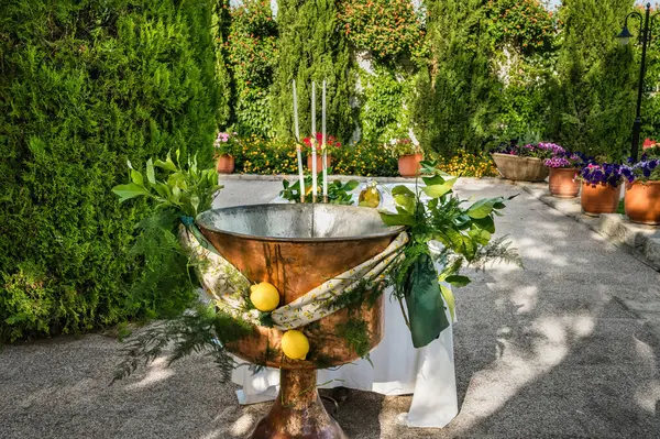 stock image Beautifully decorated copper baptismal font adorned with fresh greenery, set outdoors on sunny summer day. Font, used for Greek Orthodox baptism ceremonies.