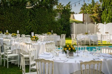 Kutlama için düzenlenmiş masalarla dolu bir yaz günü. Pırıl pırıl beyaz çarşaflar giymiş masalar, parlak mavi havuzun yanındaki yemyeşil terasta zarif bir şekilde sıralanmış. Açık hava etkinliği için mükemmel