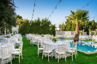 Kutlama için düzenlenmiş masalarla dolu bir yaz günü. Pırıl pırıl beyaz çarşaflar giymiş masalar, parlak mavi havuzun yanındaki yemyeşil terasta zarif bir şekilde sıralanmış. Açık hava etkinliği için mükemmel