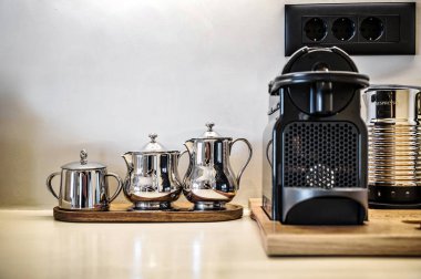 Kitchen detail. Close-up shot of modern coffee setup featuring sleek coffee machine. Next to machine, shiny stainless steel containers for milk and sugar placed. clipart