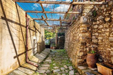Pergola 'nın duvarlara gölge düşürdüğü taştan bir sokak. Yaşlanmış taş ve yıpranmış ahşap eski dünya atmosferini yaratır. Yeşillik ve saksı bitkileri tarihsel ortama sıcaklık katar..