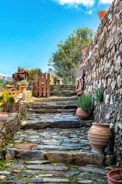 Yosun dolu taştan bir patika, ahşap kapıya çıkıyor. Terakotta kapları ve bitkileri var. Güneşli geleneksel Akdeniz köyü manzarası büyüleyici kırsal detaylar ve yemyeşil