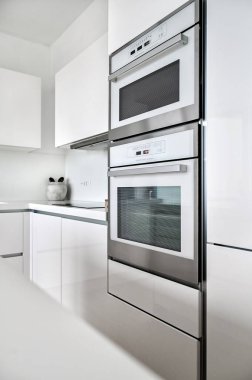 Parlak dolapları olan çağdaş beyaz mutfak, dahili mikrodalga fırın, minimalist dekor, modern aletler, parlak bir dekor ve temiz tezgahlar..