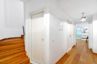 Beyaz duvarlı modern koridor, ahşap döşeme ve minimalist tasarım. Merdiven ve kapılar çağdaş iç mekanlarda temiz çizgiler ve simetri yaratır.