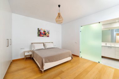 Minimalist yatak odası, çift kişilik yatak odası, beyaz duvarlar, ahşap zemin, soyut sanat eseri, kolye ışığı, buzlu cam banyo kapısı, şık, temiz tasarım, rahat atmosfer..