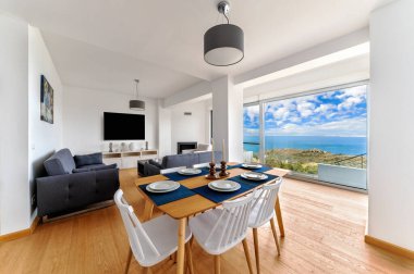 Çağdaş yemek ve yaşam alanı panoramik deniz manzaralı, ahşap zemin, büyük pencereler, minimalist dekor, zarif modern mobilyalar..