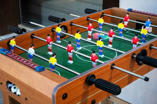 Klasik ahşap langırt masası. Renkli oyuncu figürleri yeşil sahada oyun pozisyonlarına dizilmiş. Masaüstü oyun sahnesi çubuklar, kulplar ve minyatür futbol unsurlarında ayrıntıları gösterir.