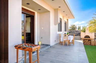 Arka bahçe manzaralı langırt masası, yemek alanı, barbekü fırını ve parlak gökyüzü. Modern villada eğlence, yemek ve açık hava eğlencesi için mükemmel bir aile ortamı..