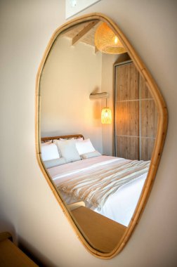 Yatak odasının, yumuşak yatak odasının, ahşap gardırobun ve sıcak ışığın ayna yansıması. Bohem aksanlı minimal iç tasarım sakin ve rahatlatıcı atmosfer yaratır..