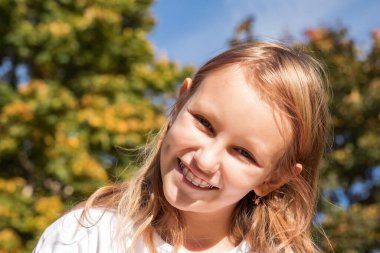 Gülümseyen neşeli kız 8-9 yaşlarında, ortodontik aletli, doğada bir çocuğun yakın plan portresi.