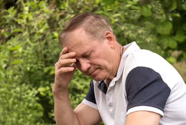 stock image portrait of a mature man, 50-60 years old, sitting with his eyes closed in deep thought, hand on his head