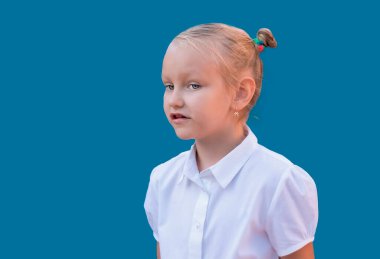 Mavi arka planda beyaz bluzlu Avrupalı ilkokul öğrencisi kız, 7 yaşında sinsi bakışlı bir sarışın portresi.